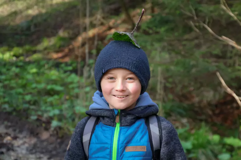 Junge mit Blatt am Kopf im Wald