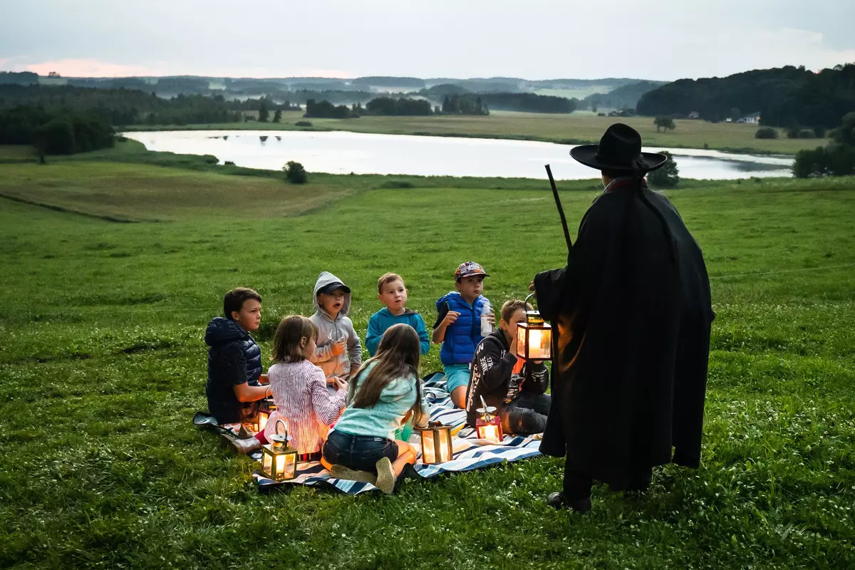 Guide mit Laterne und einer Gruppe von Kindern auf einer Wiese in der Dämmerung