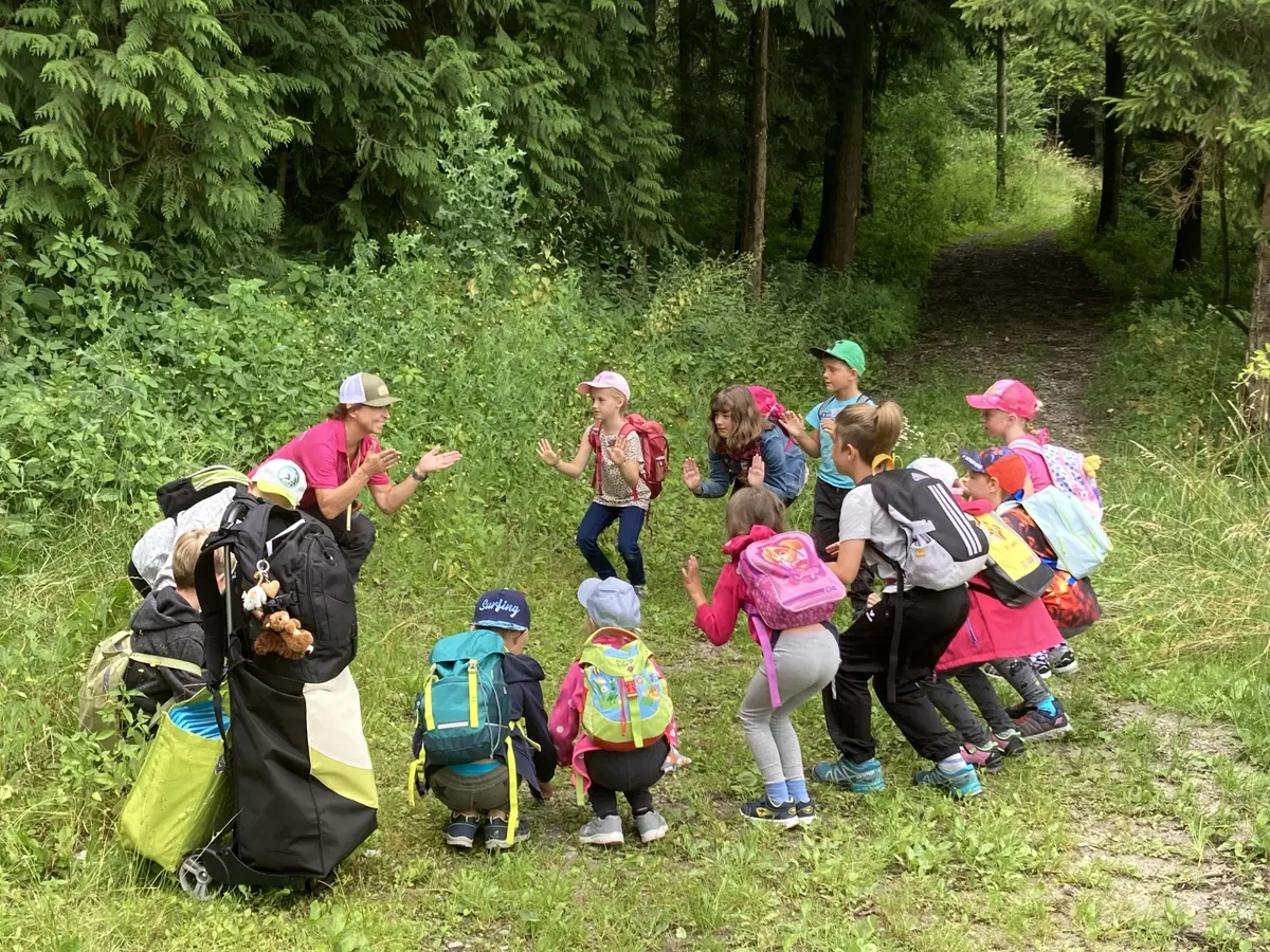 Guide führt mit einer Gruppe von Kindern Übungen im Wald durch