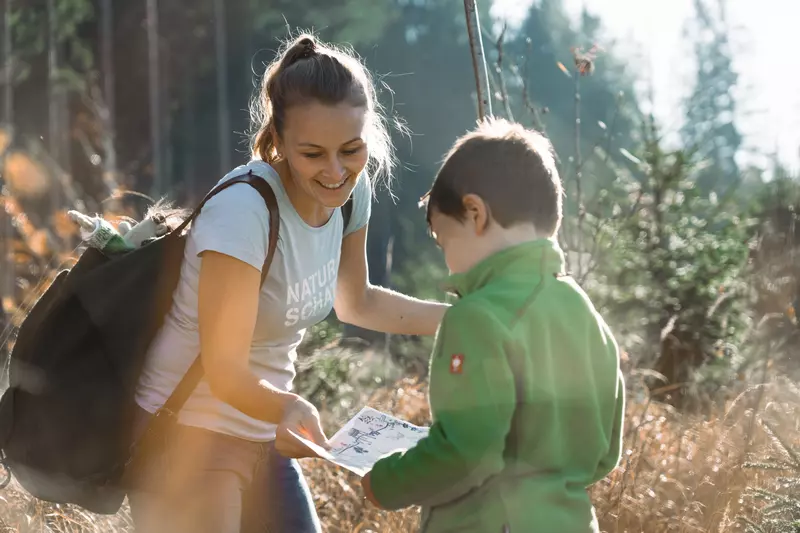 Guide und Junge schauen in einer Waldlichtung auf eine Karte