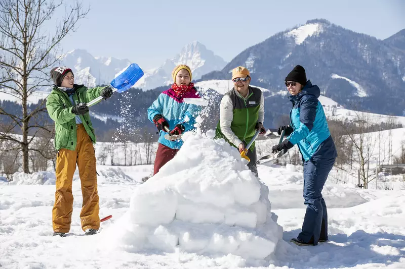 Familie an 4 Personen steht um einen Schneehaufen und wirft Schnee in die Luft