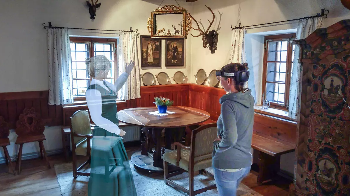 Zwei Frauen in altem Esszimmer, eine hat VR Brille, die andere ist durchsichtig