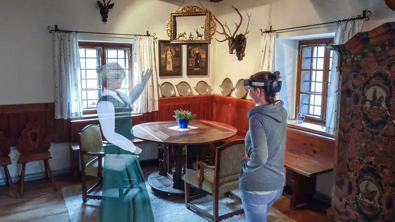 Zwei Frauen in altem Esszimmer, eine hat VR Brille, die andere ist durchsichtig