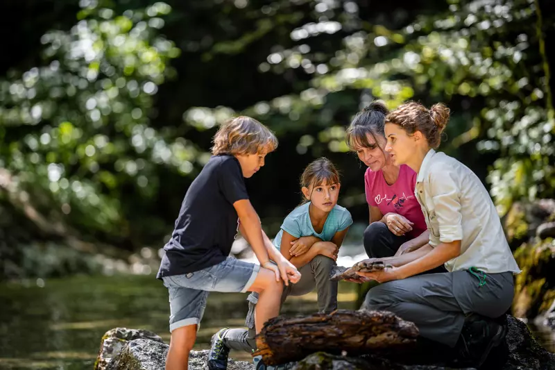 Rangerin hält Holzstück in den Händen, daneben zwei Kinder und eine Frau