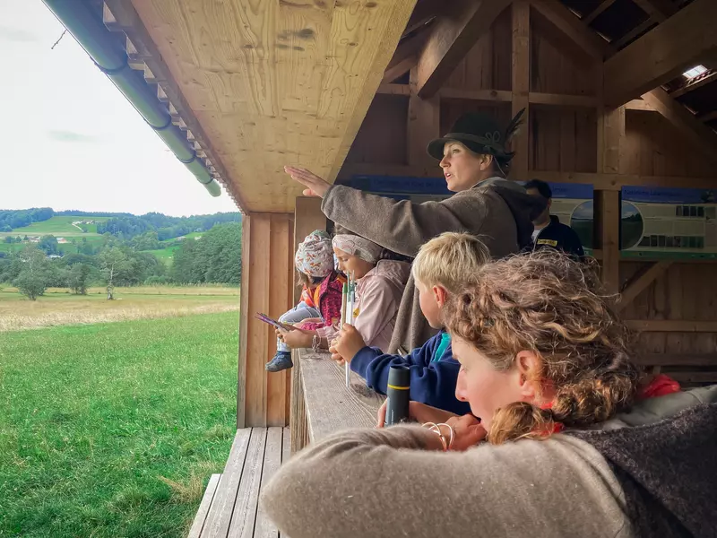 Guide erklärt Kindern von einer Holzhütte aus die umliegende Landschaft