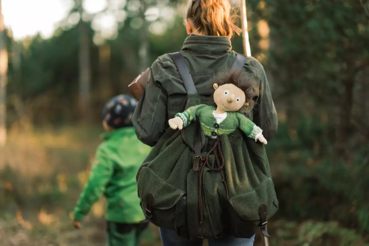 Guide mit Plüschtier in einem Wanderrucksack auf einem Waldpfad