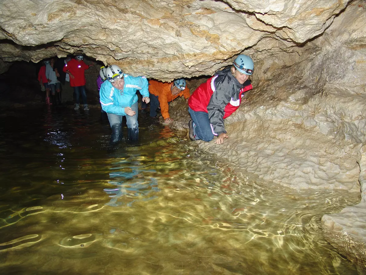 Gruppe wandert durch Höhle, eine Frau steht knietief im Wasser