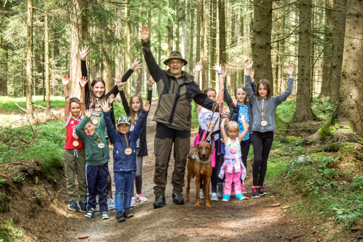 Guide mit Kindergruppe jubelnd im Wald