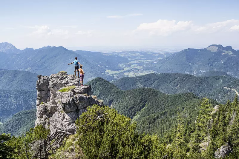 Zwei Personen stehen auf Felserhöhung mit Blick über den darunter liegenden Wald