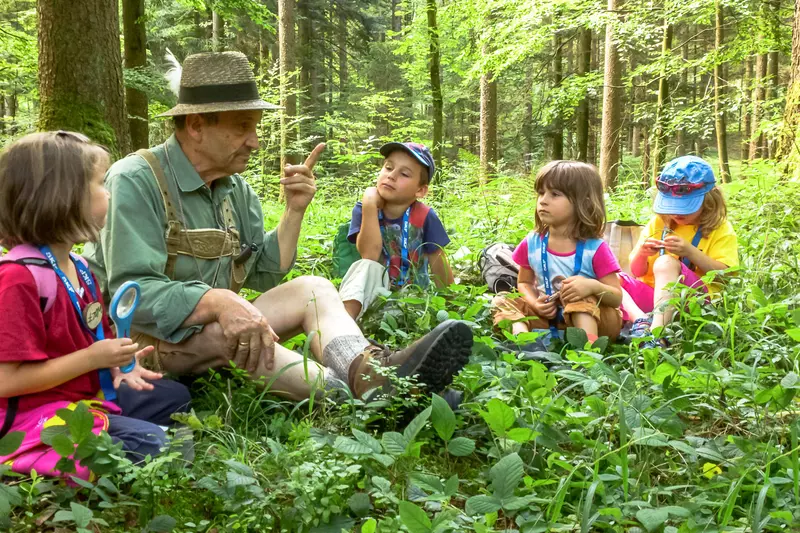 Guide mit Kindergruppe sitzt am Waldboden.