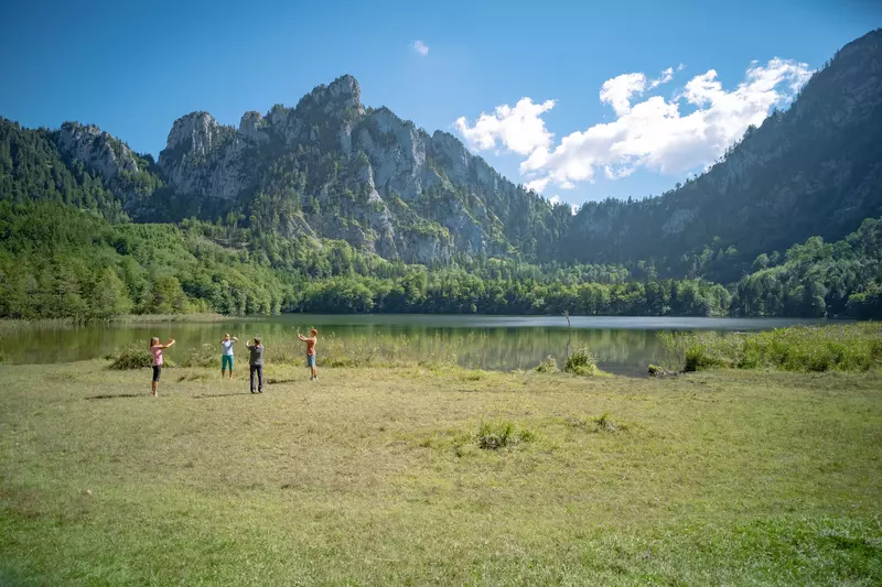 Gruppe von Teilnehmenden macht zusammen mit Guide Übungen auf einer Wiese neben einem Bergsee