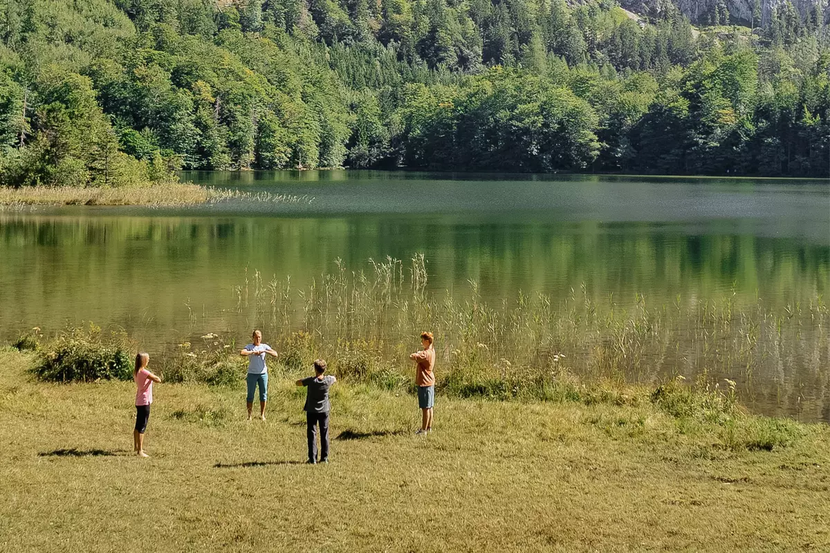 Gruppe von Teilnehmenden macht zusammen mit Guide Übungen auf einer Wiesen neben einem Bergsee