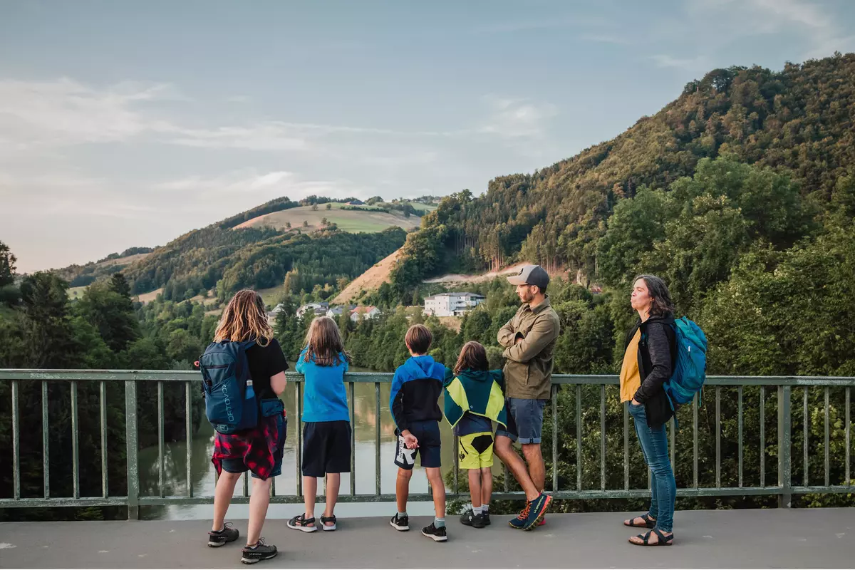 Gruppe von Teilnehmenden mit Kindern auf einer Brücke über einem Fluss in der Dämmerung