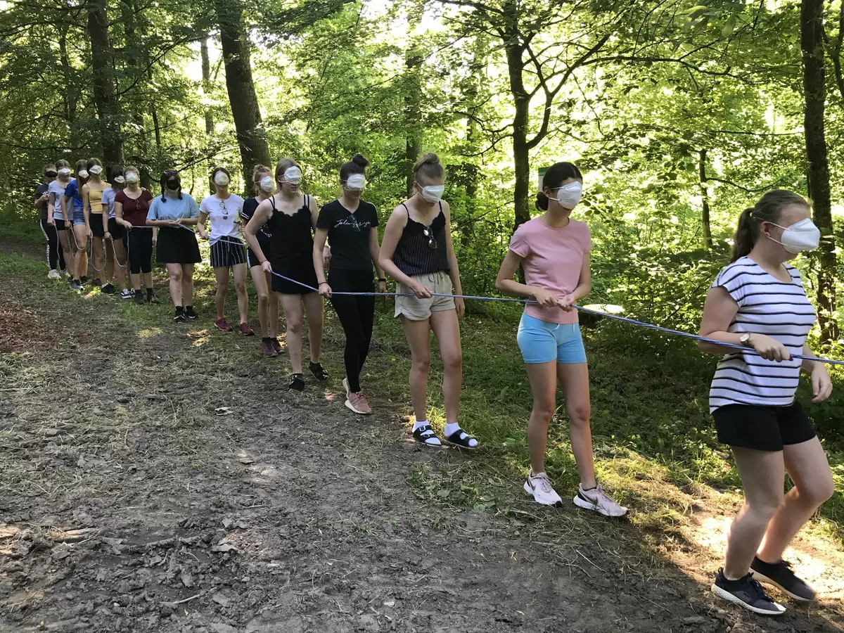 Schülergruppe wandert blind, an einem Seil in der Reihe durch den Wald