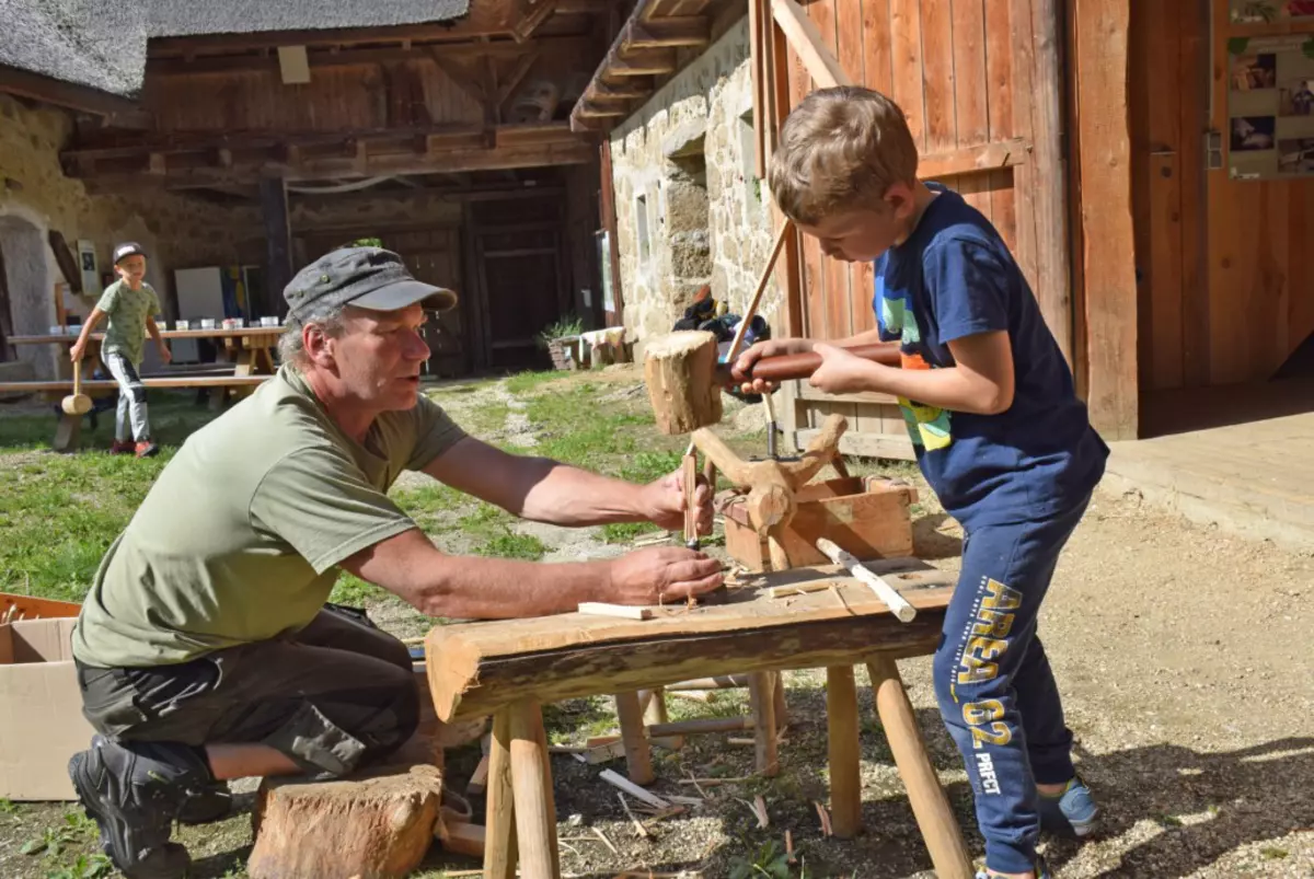 Ein Bub mit historischem Holzhammer hämmert Holz, der Guide unterstützt ihn dabei