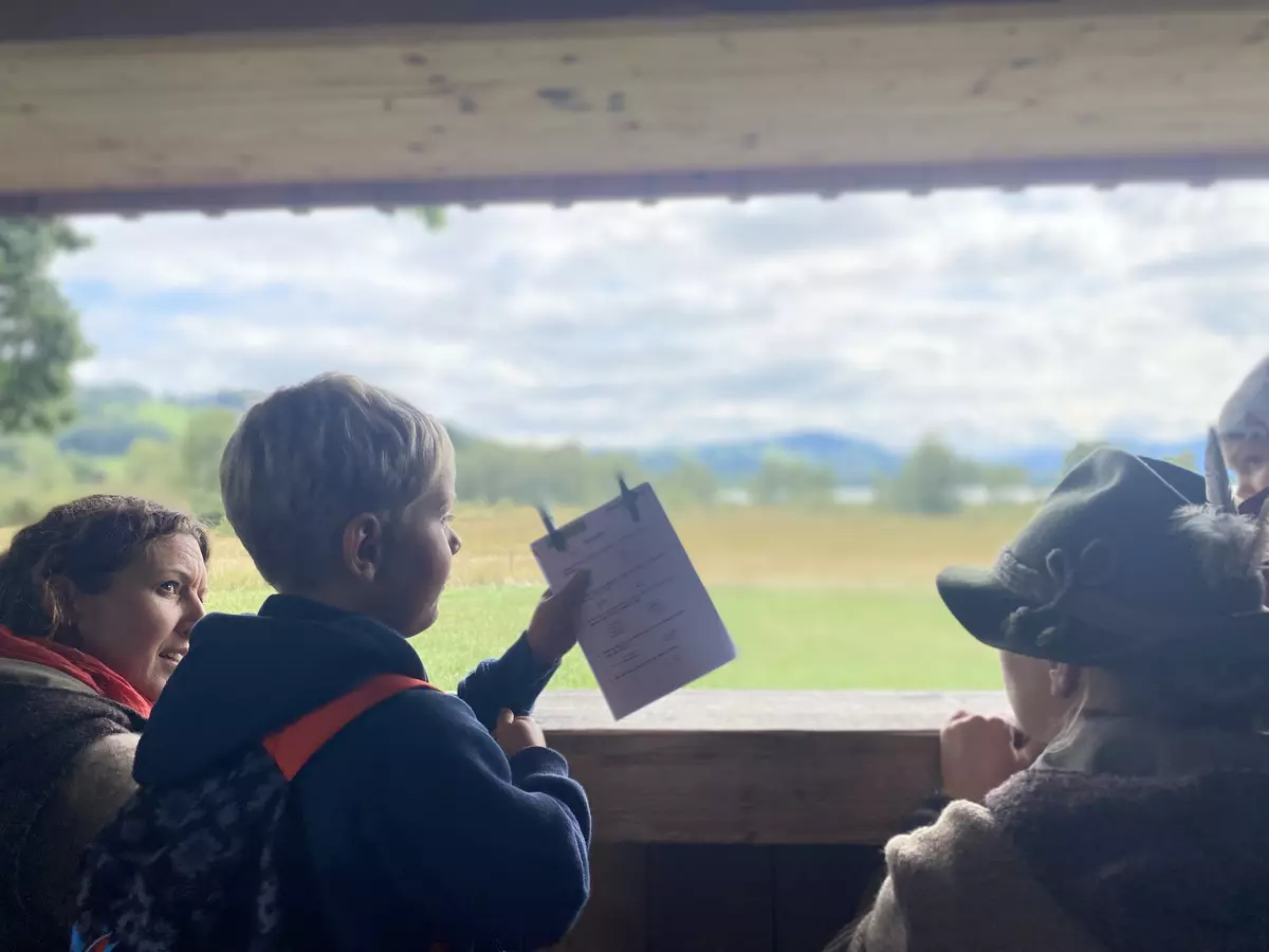 Kind blickt zusammen mit Guide aus einer Holzhütte auf die Landschaft