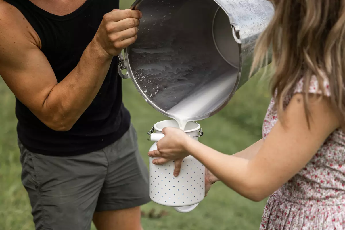 Guide und Mädchen füllen frische Milch aus einem Eimer in eine Milchkanne