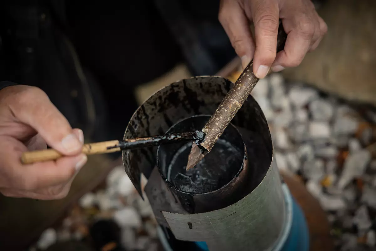 Teilnehmender bepinselt ein spitzes Stück Holz mit Pech