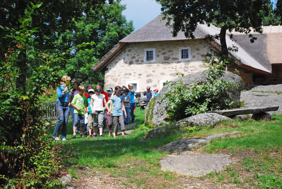 Eine Gruppe von Kindern mit Augenbinden vor einem Steinhaus in der Wiese
