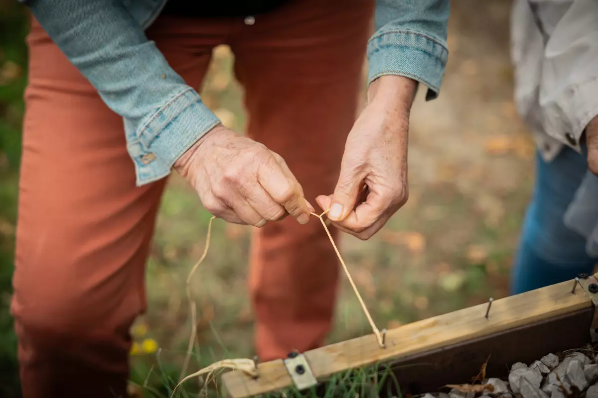 Teilnehmende bindet Faden an ein Stück Holz