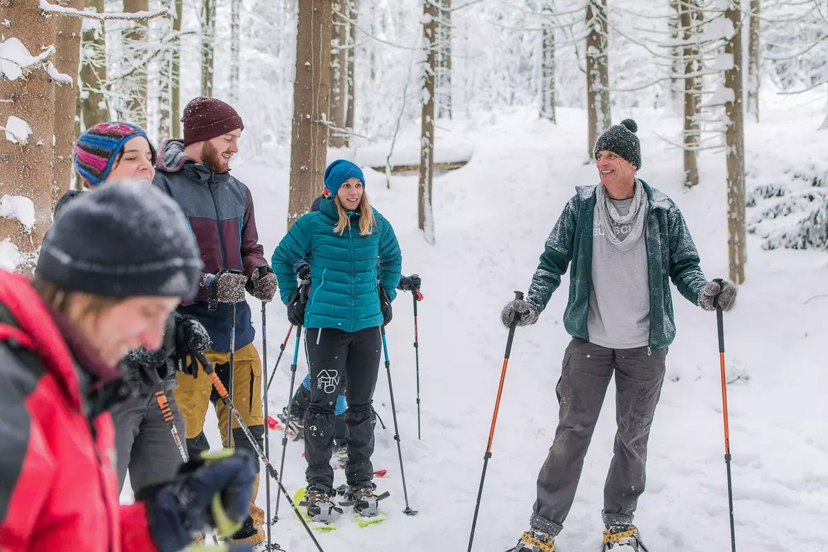 Guide steht mit Gruppe im Wald auf Schneeschuhen