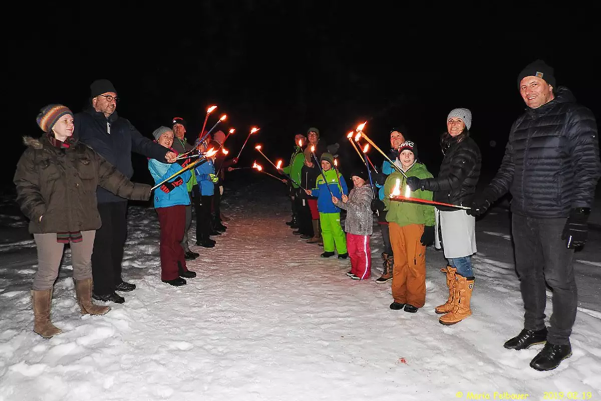 Erwachsene und Kinder mit Fackeln in der Nacht auf schneebedecktem Weg