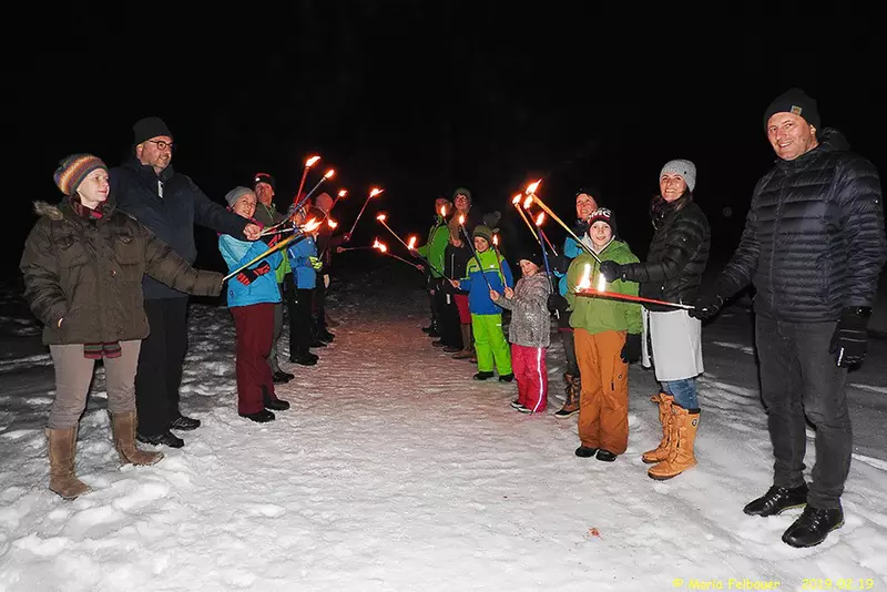 Erwachsene und Kinder mit Fackeln in der Nacht auf schneebedecktem Weg