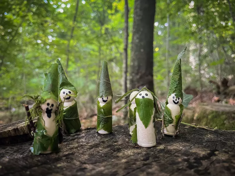 Gebastelte Waldmännchen aus Blättern auf einem Baumstamm stehend.