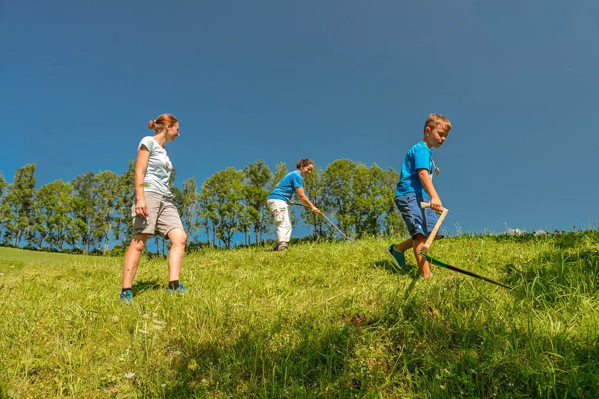 Der Guide zeigt zwei Kindern das Mähen mit Sense.