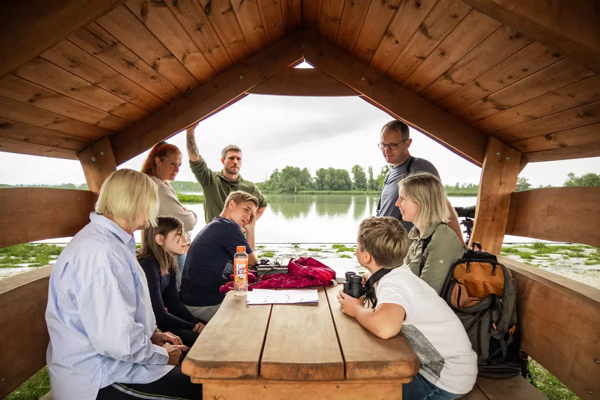 Gruppe sitzt mit Guide in einer Hütte am Ufer